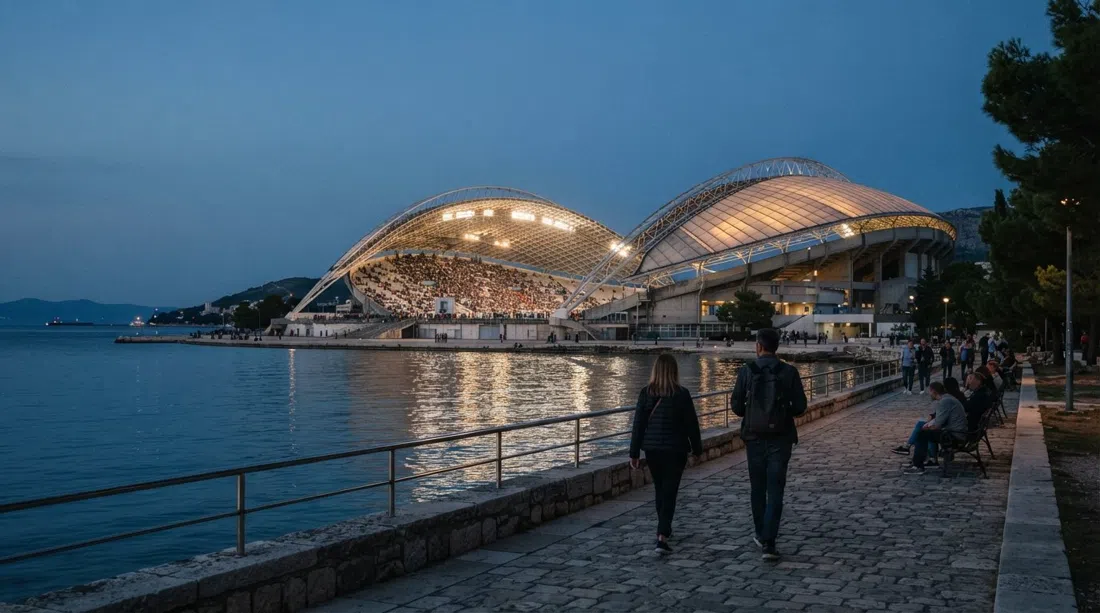 Estadio Poljud en Split al anochecer, el techo con forma de caparazón brillando sobre la bahía con el graderío visible a través de la estructura abierta